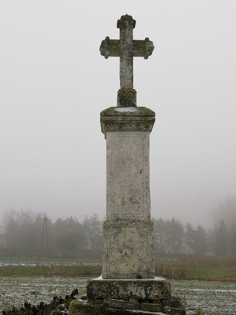 Krzyż murowany na postumencie, zlokalizowany w pobliżu chodnika łączącego 