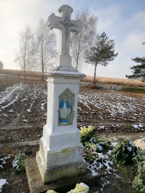 Kapliczka słupowa z krzyżem murowana po lewej stronie drogi powiatowej w stronę Wojciechowice przed łukiem tej drogi z napisem „KROLOWO KORONY POLSKIEJ MÓDL SIĘ ZA NAMI”