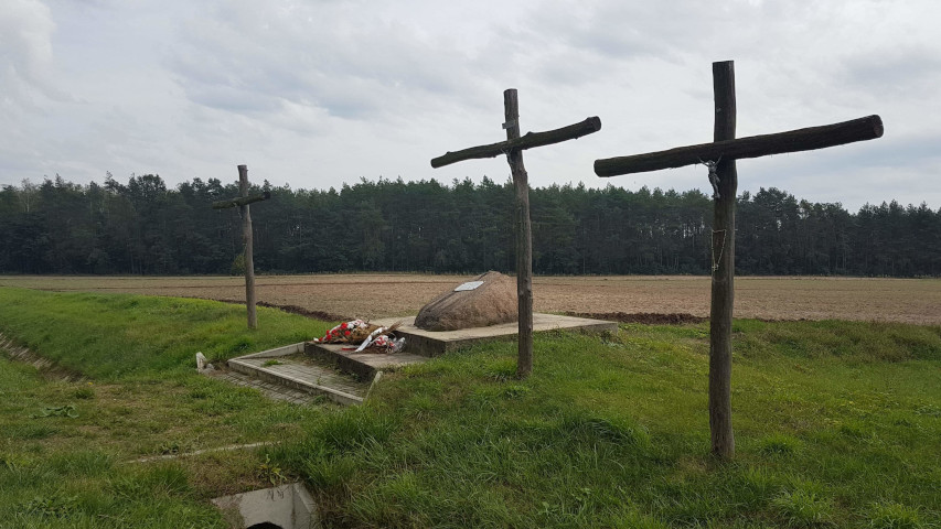 Trzy drewniane krzyże przy drodze wojewódzkiej Nr DW755 po prawej stronie w kierunku Ożarowa. Na głazie tablica z inskrypcją: W tym miejscu dn. 25 sierpnia 1943 oddział partyzancki NOW wachm. 