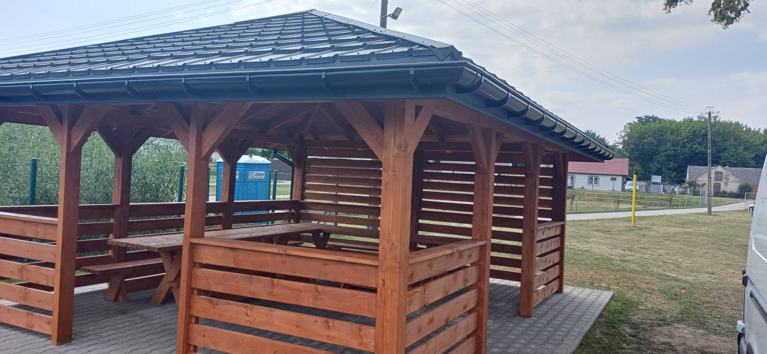 Odbiór altanki z wyposażeniem przy stadionie sportowym w Wojciechowicach Drewniana brązowa altana z blaszanym dachem i rynnami w kolorze czarnym