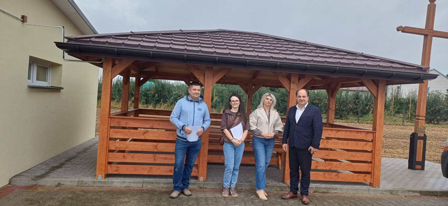 Odbiór altanki z wyposażeniem przy świetlicy wiejskiej w Orłowinach Od lewej wykonawca altany, pracownik Urzędu Gminy, Sołtys Orłowin oraz Wójt Gminy na tle drewnianej altany