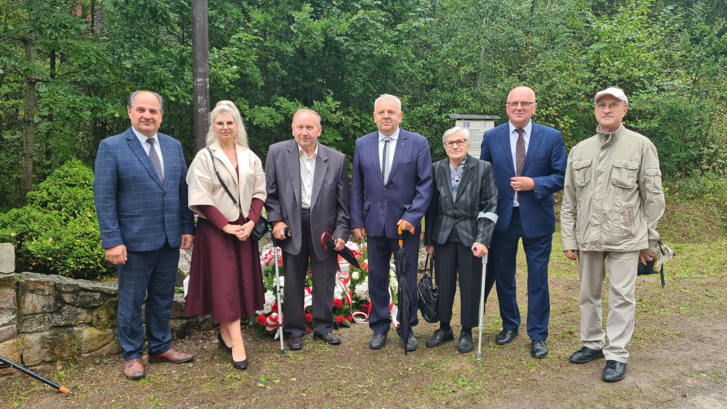 Zdjęcie grupowe w miejscu pamięci, w tle wiązanki i las
