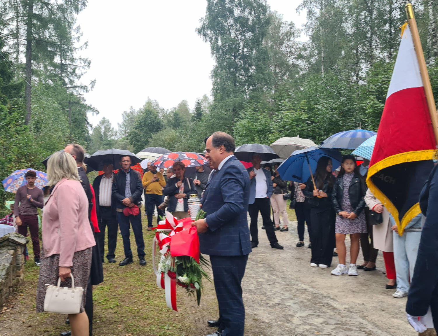 Wójt Gminy Wojciechowice z wiązanką w ręce, w tle zgromadzeni ludzie na uroczystości