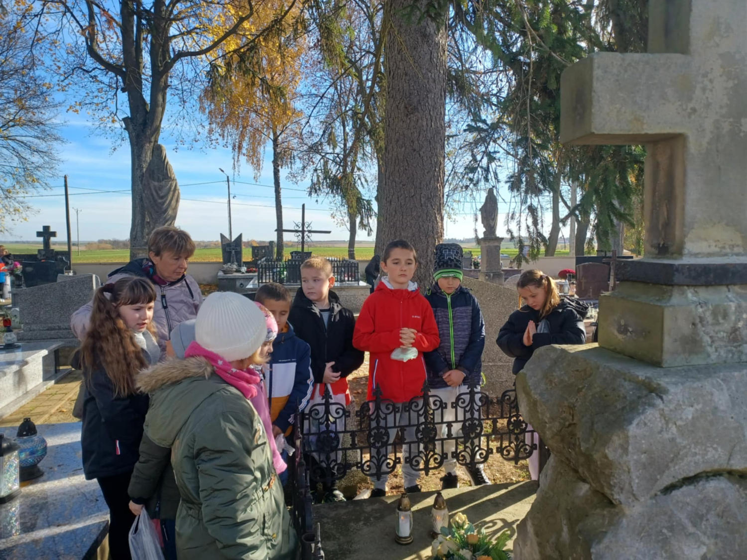 Zdjęcie 1 Uczniowie wraz z nauczycielką przed mogiłą z krzyżem